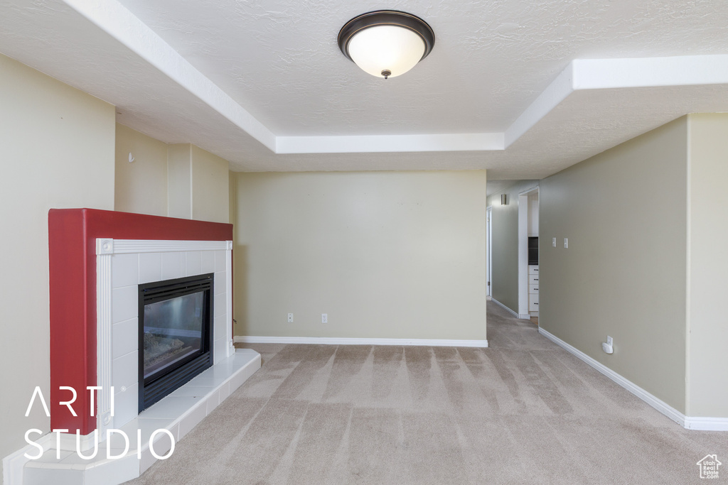 Unfurnished living room featuring carpet flooring, a raised ceiling, baseboards, and a textured ceiling