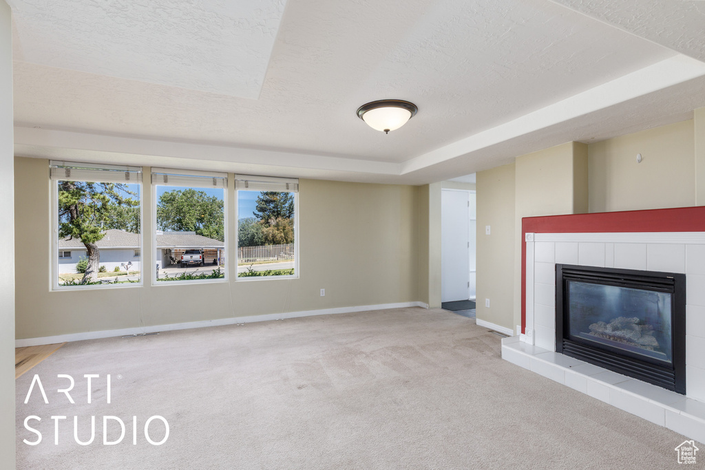 Unfurnished living room featuring carpet, a textured ceiling, a fireplace, plenty of natural light, and a tray ceiling