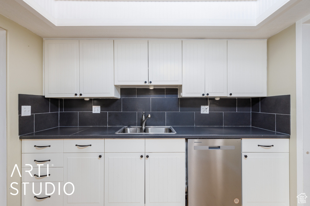 Kitchen featuring stainless steel dishwasher, a sink, dark countertops, and backsplash