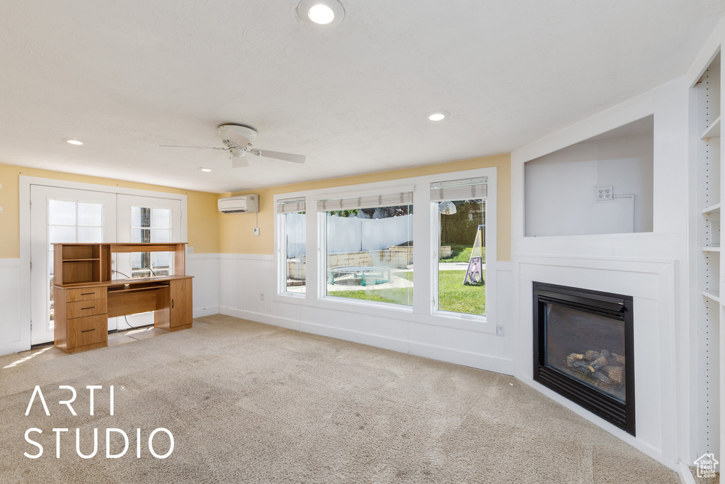 Unfurnished living room with a wall mounted air conditioner, carpet floors, ceiling fan, wainscoting, and a glass covered fireplace