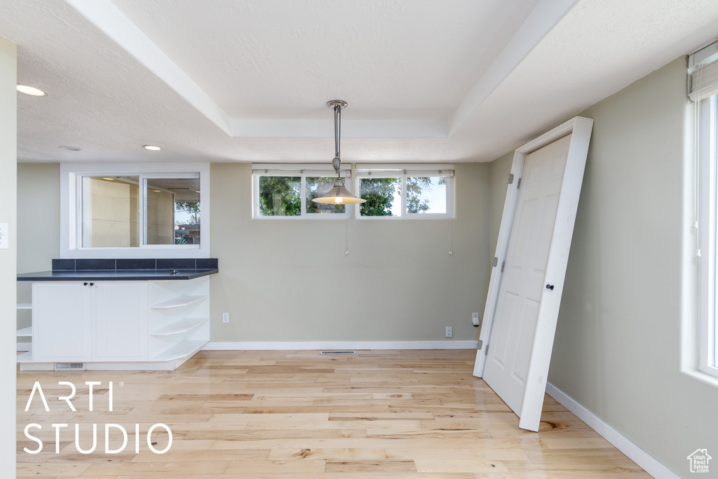 Unfurnished dining area with light wood finished floors, baseboards, recessed lighting, and a raised ceiling