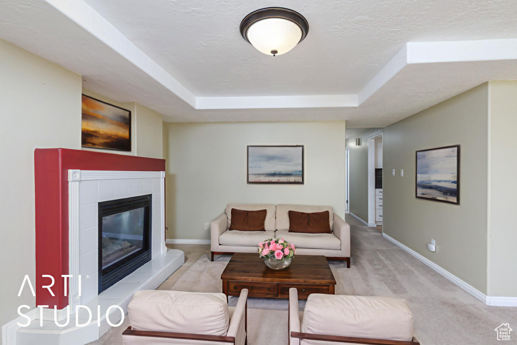 Living room featuring baseboards, a raised ceiling, a tiled fireplace, a textured ceiling, and light carpet