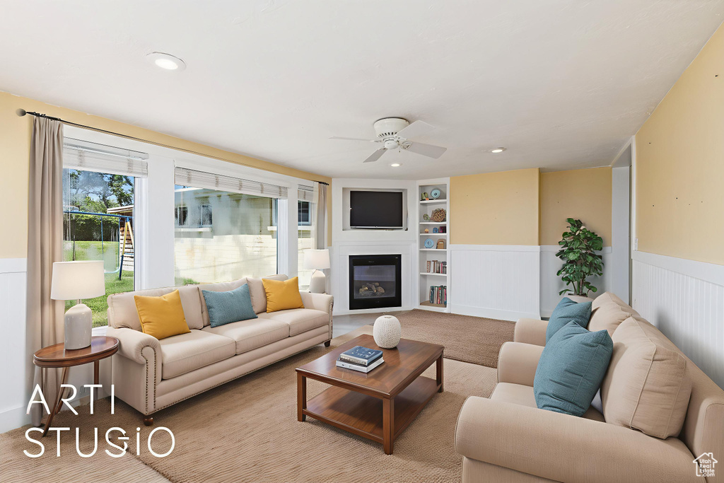 Carpeted living area featuring built in features, a ceiling fan, a wainscoted wall, a glass covered fireplace, and recessed lighting