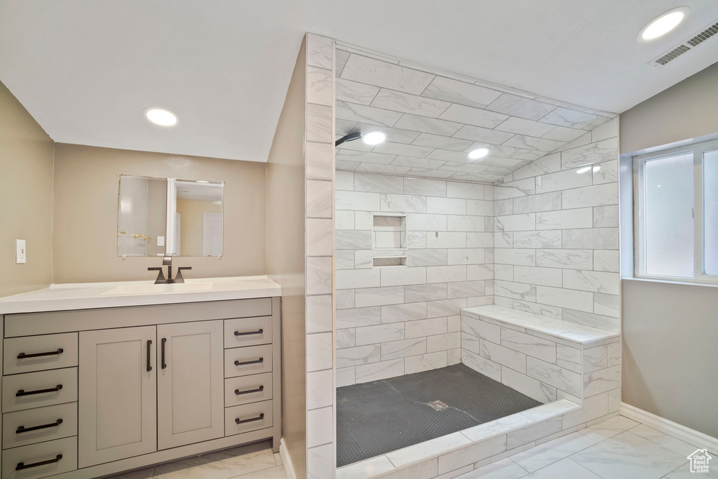 Full bath featuring marble finish floors, tiled shower, vanity, baseboards, and vaulted ceiling