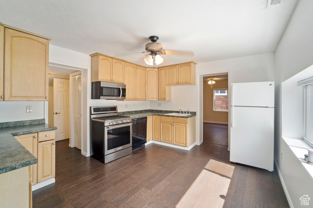 Kitchen with appliances with stainless steel finishes, light brown cabinetry, ceiling fan, a sink, and dark countertops