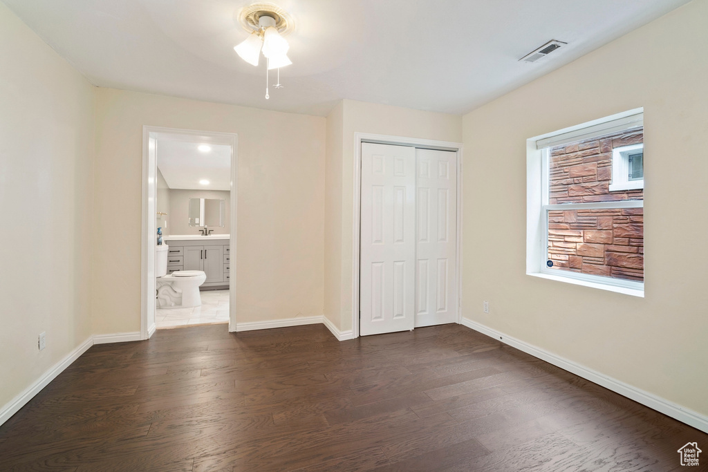 Unfurnished bedroom featuring dark wood-style flooring, baseboards, a closet, and connected bathroom