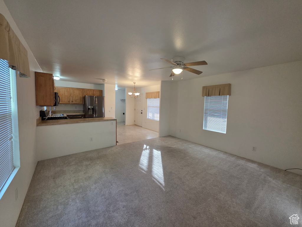 Unfurnished living room featuring a chandelier, a ceiling fan, and light colored carpet
