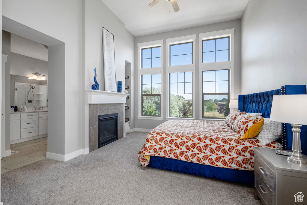 Bedroom with carpet floors, ensuite bathroom, a tile fireplace, baseboards, and a ceiling fan