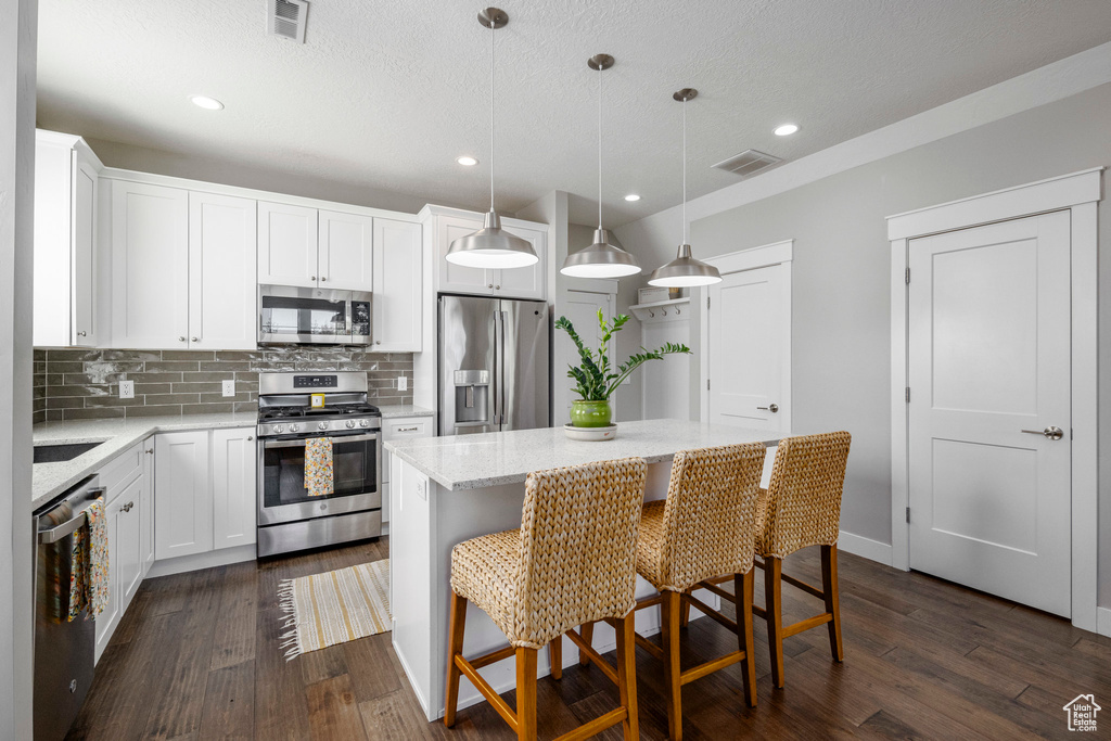 Kitchen with appliances with stainless steel finishes, decorative backsplash, a center island, dark wood-type flooring, and decorative light fixtures