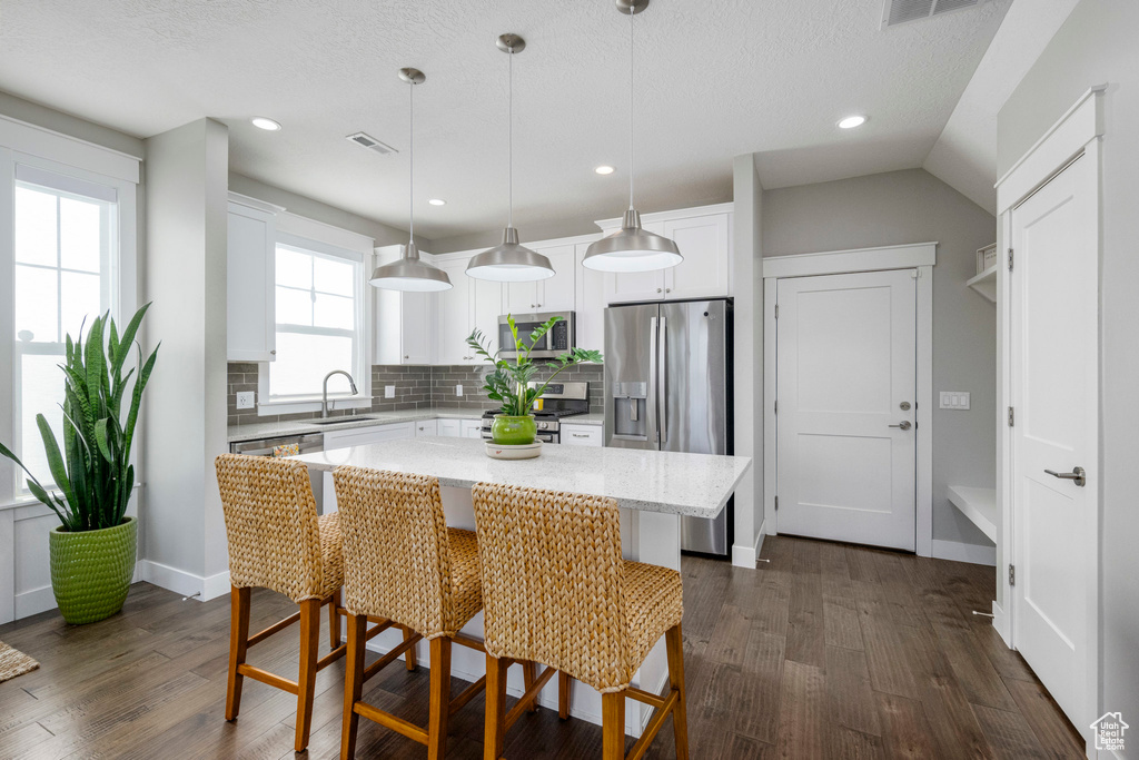 Kitchen featuring stainless steel appliances, a sink, decorative backsplash, dark wood-type flooring, and white cabinetry