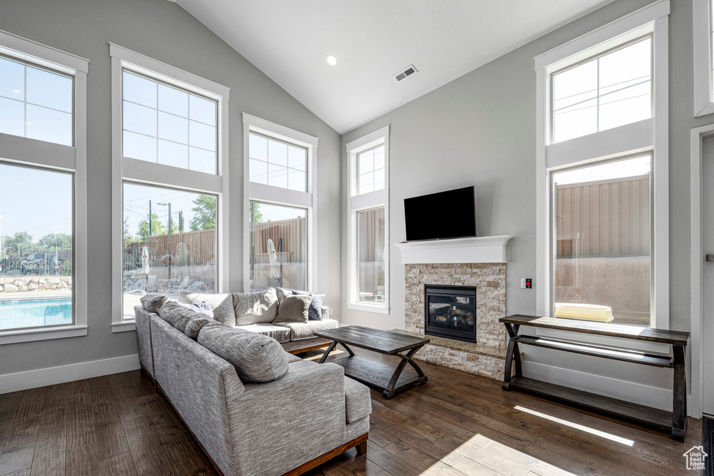 Living room with high vaulted ceiling, plenty of natural light, a fireplace, and dark wood-style flooring