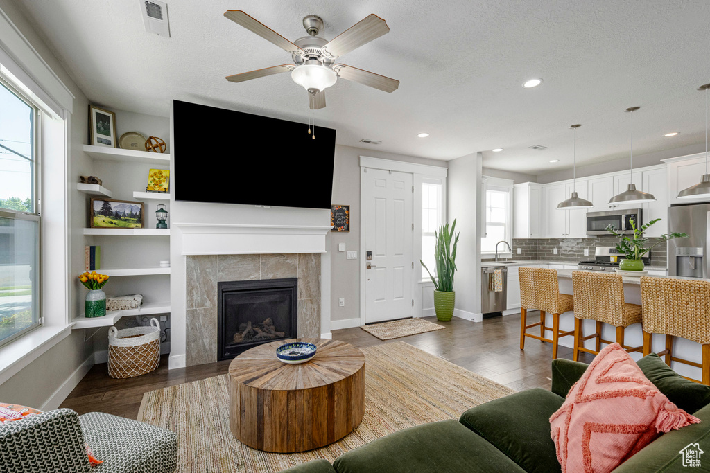 Living area featuring dark wood-type flooring, a tile fireplace, a ceiling fan, recessed lighting, and baseboards