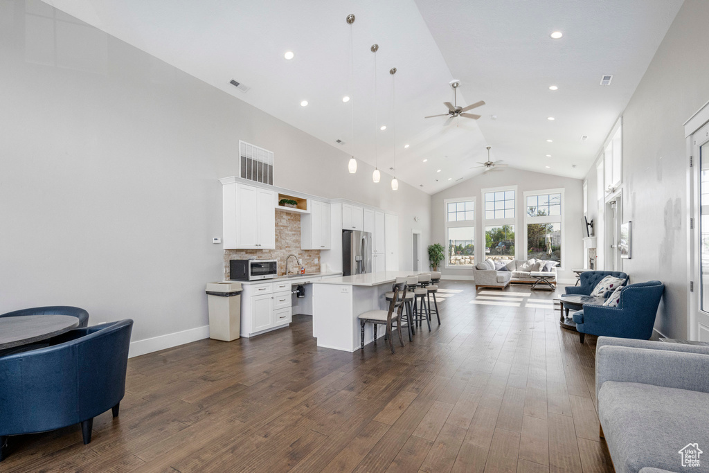 Living area featuring ceiling fan, high vaulted ceiling, dark wood-style flooring, recessed lighting, and baseboards