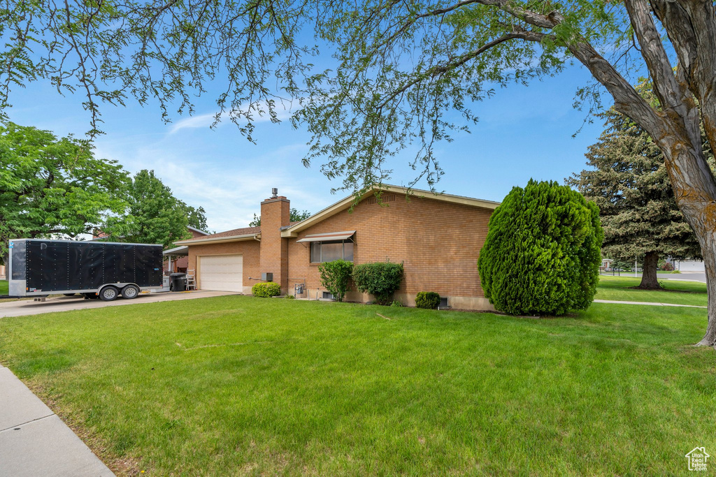 Single story home with a garage, a chimney, a front lawn, concrete driveway, and brick siding
