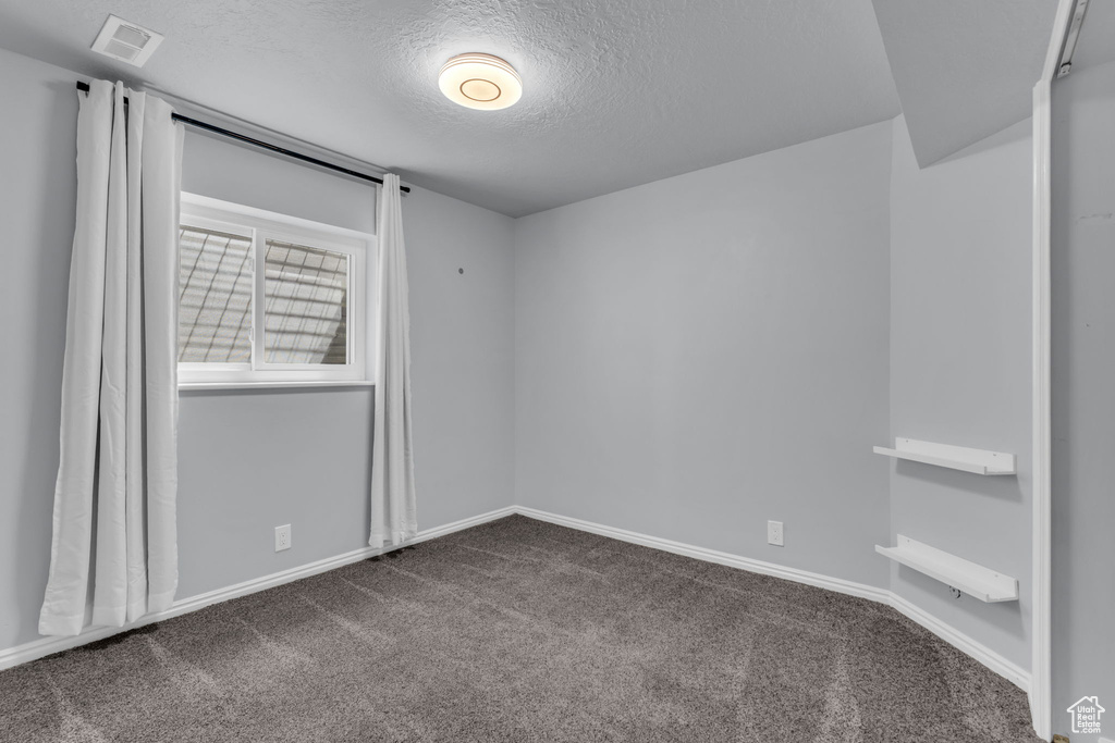 Empty room with a textured ceiling, dark colored carpet, and baseboards