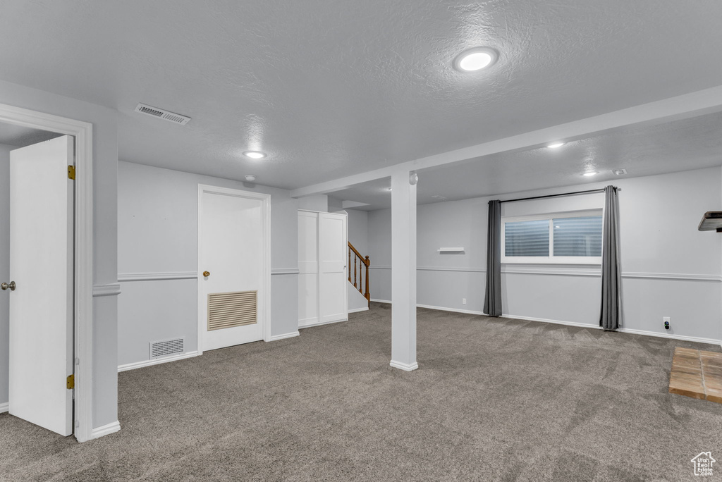 Finished below grade area with carpet flooring, baseboards, a textured ceiling, and stairway