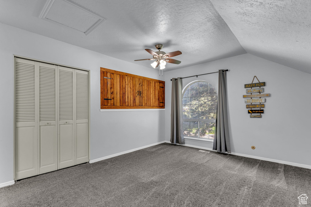 Unfurnished bedroom with vaulted ceiling, a textured ceiling, attic access, carpet flooring, and a closet