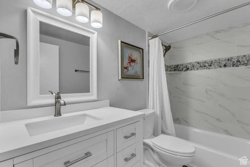 Full bath featuring toilet, shower / bath combo, vanity, and a textured ceiling