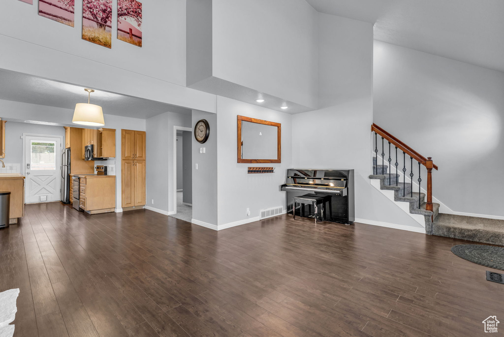Living area featuring a towering ceiling, dark wood-style floors, stairs, and baseboards