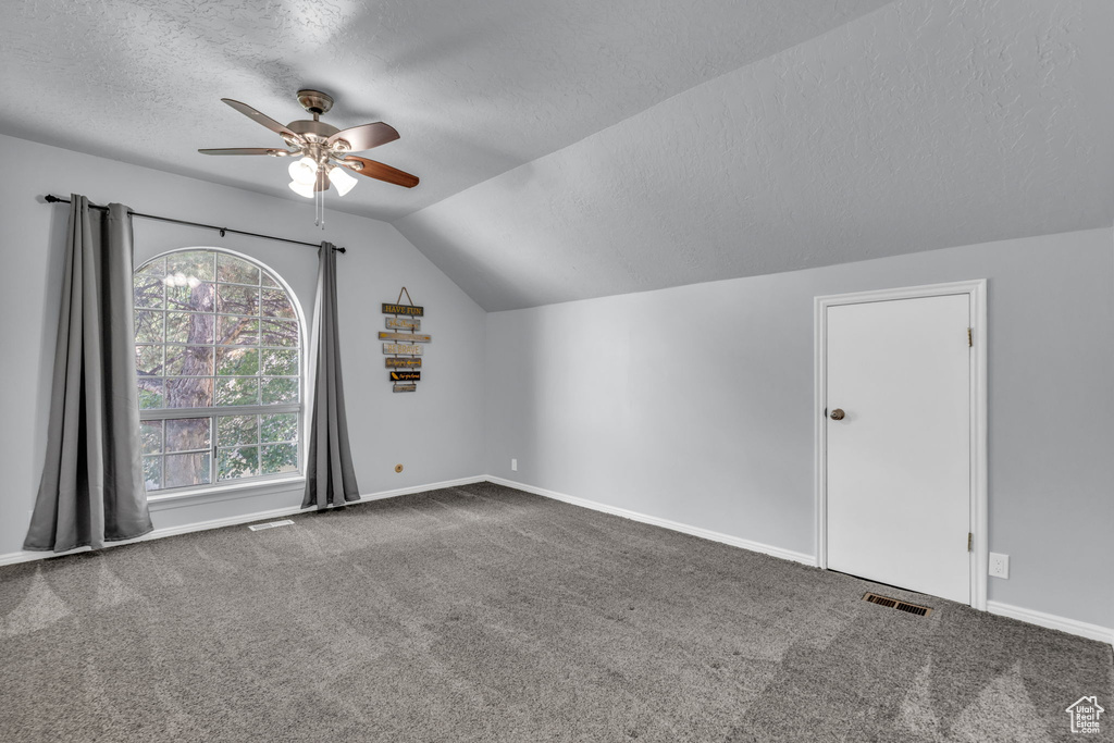 Bonus room with a textured ceiling, a ceiling fan, vaulted ceiling, carpet, and baseboards