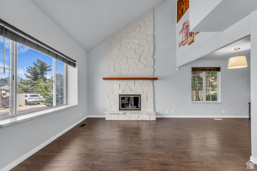 Unfurnished living room featuring high vaulted ceiling, wood finished floors, a stone fireplace, and baseboards
