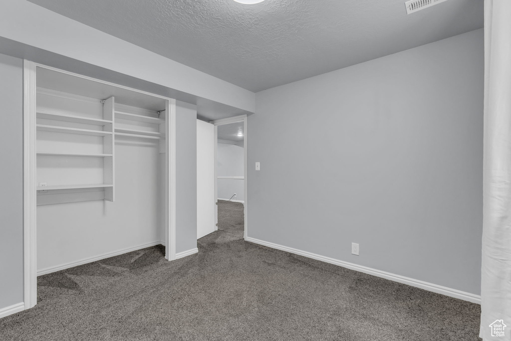 Unfurnished bedroom with dark colored carpet, baseboards, a textured ceiling, and a closet
