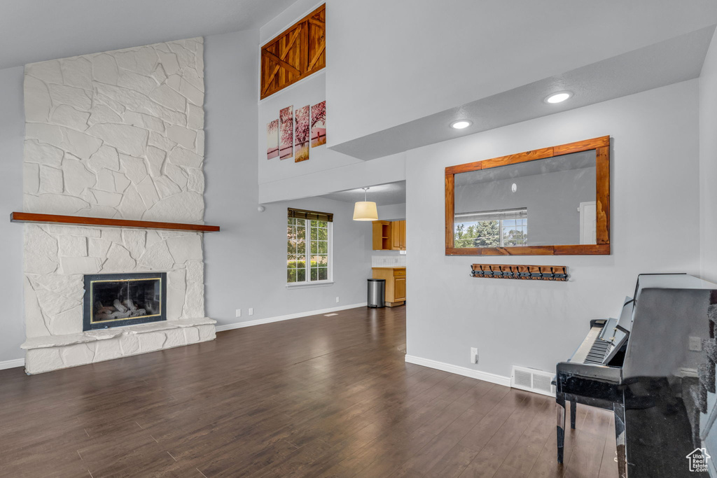Living room featuring a towering ceiling, wood finished floors, baseboards, a stone fireplace, and recessed lighting