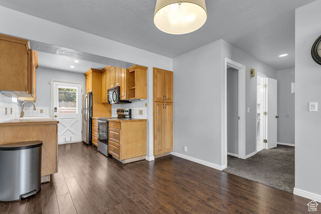 Kitchen featuring stainless steel appliances, light countertops, baseboards, dark wood-style flooring, and a sink