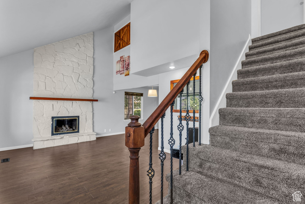 Stairway with high vaulted ceiling, wood finished floors, baseboards, and a fireplace