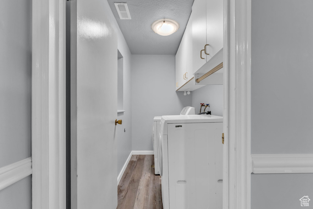 Washroom with wood finished floors, cabinet space, washing machine and dryer, baseboards, and a textured ceiling