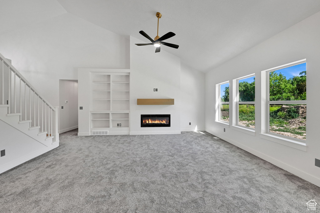 Unfurnished living room with high vaulted ceiling, ceiling fan, carpet, a glass covered fireplace, and baseboards