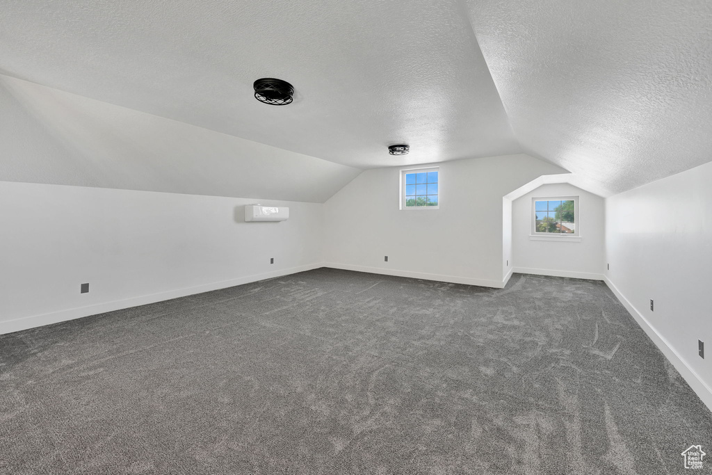 Additional living space featuring a textured ceiling, lofted ceiling, baseboards, and dark carpet