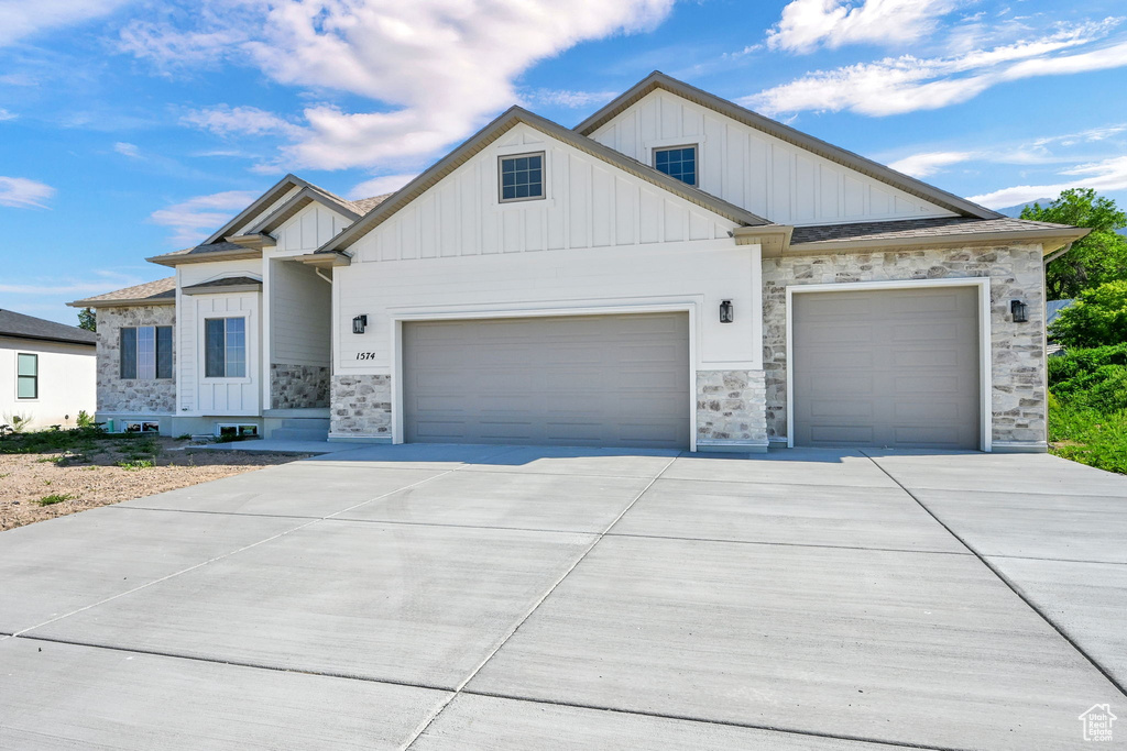 View of front of property with board and batten siding, a garage, stone siding, and concrete driveway