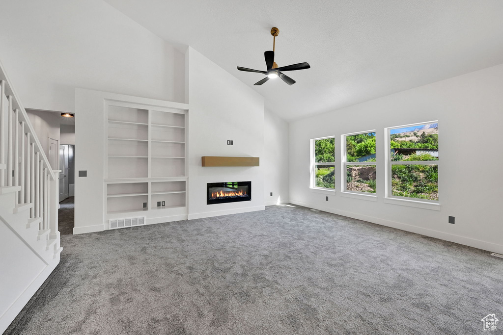 Unfurnished living room featuring high vaulted ceiling, a glass covered fireplace, a ceiling fan, stairway, and carpet floors