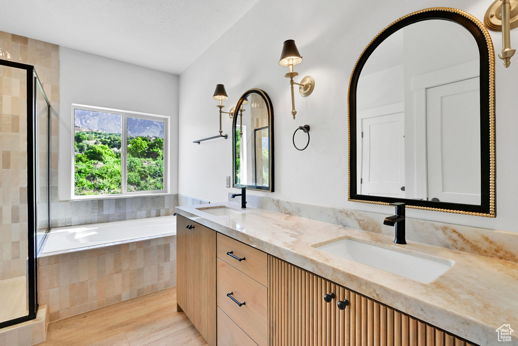 Bathroom featuring a shower stall, double vanity, a garden tub, and wood finished floors