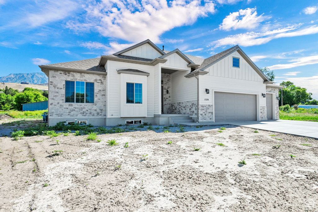 View of front of home with an attached garage, board and batten siding, concrete driveway, and stone siding