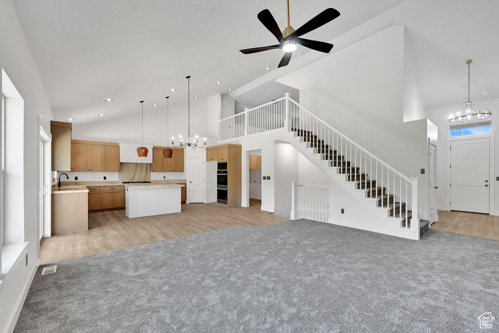 Unfurnished living room with a chandelier, high vaulted ceiling, light colored carpet, stairway, and recessed lighting