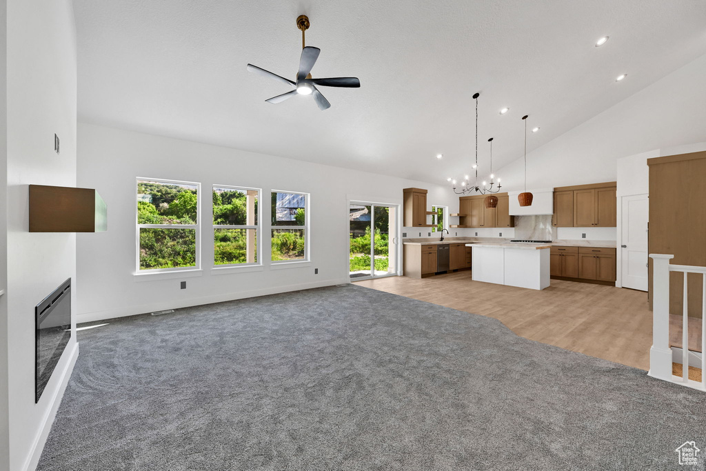 Unfurnished living room featuring light carpet, a ceiling fan, high vaulted ceiling, a chandelier, and recessed lighting