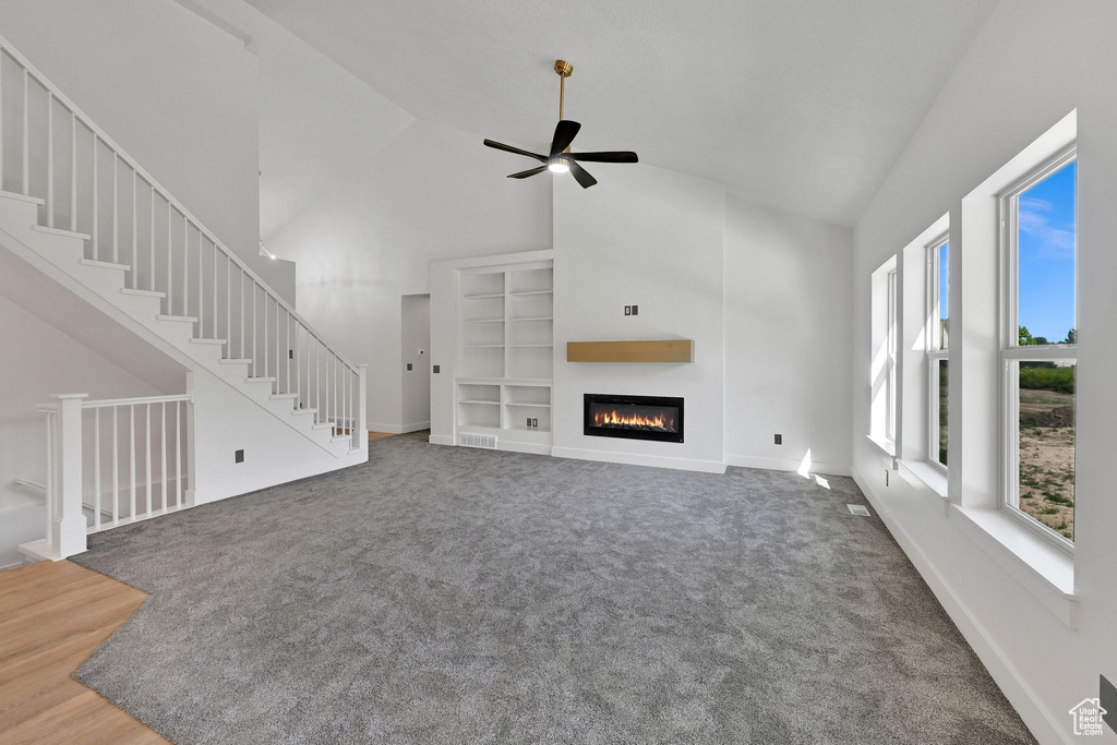 Unfurnished living room featuring high vaulted ceiling, carpet flooring, a glass covered fireplace, ceiling fan, and baseboards