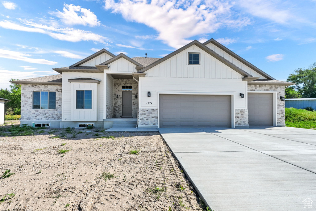 Modern farmhouse featuring board and batten siding, a garage, driveway, and stone siding