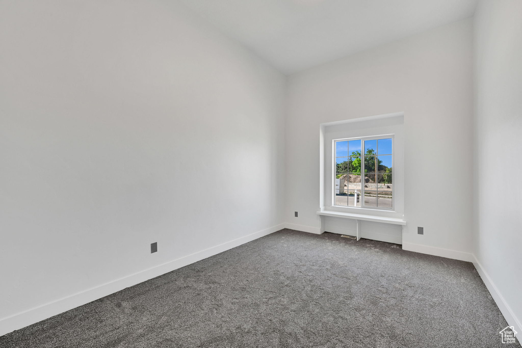 Unfurnished room featuring dark colored carpet and baseboards