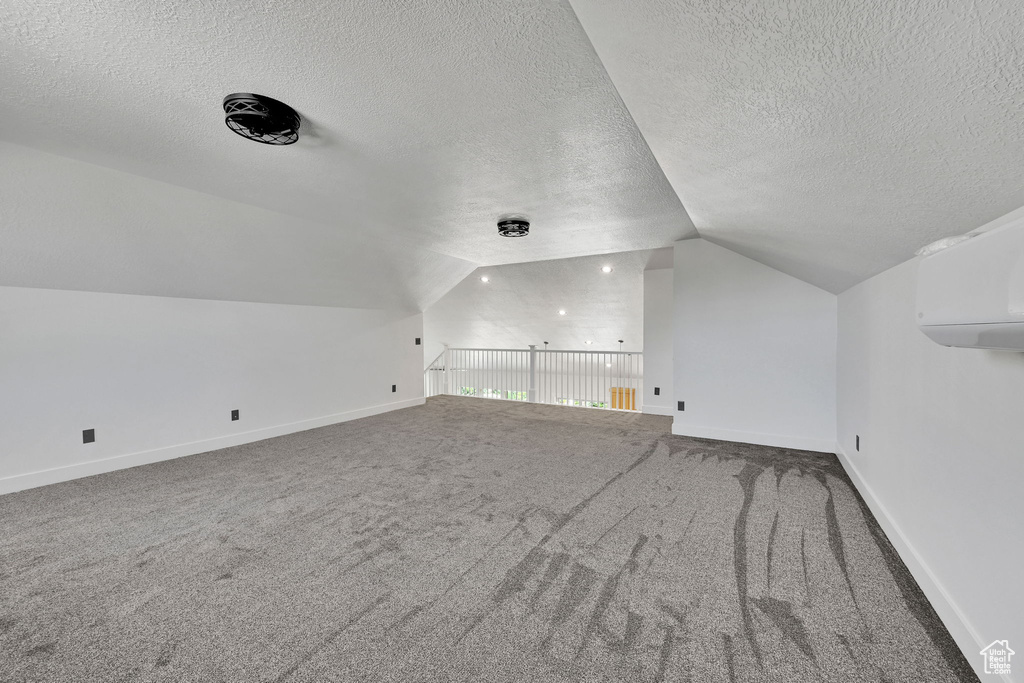Bonus room with vaulted ceiling, a textured ceiling, carpet, baseboards, and a wall unit AC