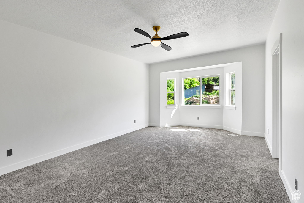 Carpeted empty room with a ceiling fan, a textured ceiling, and baseboards