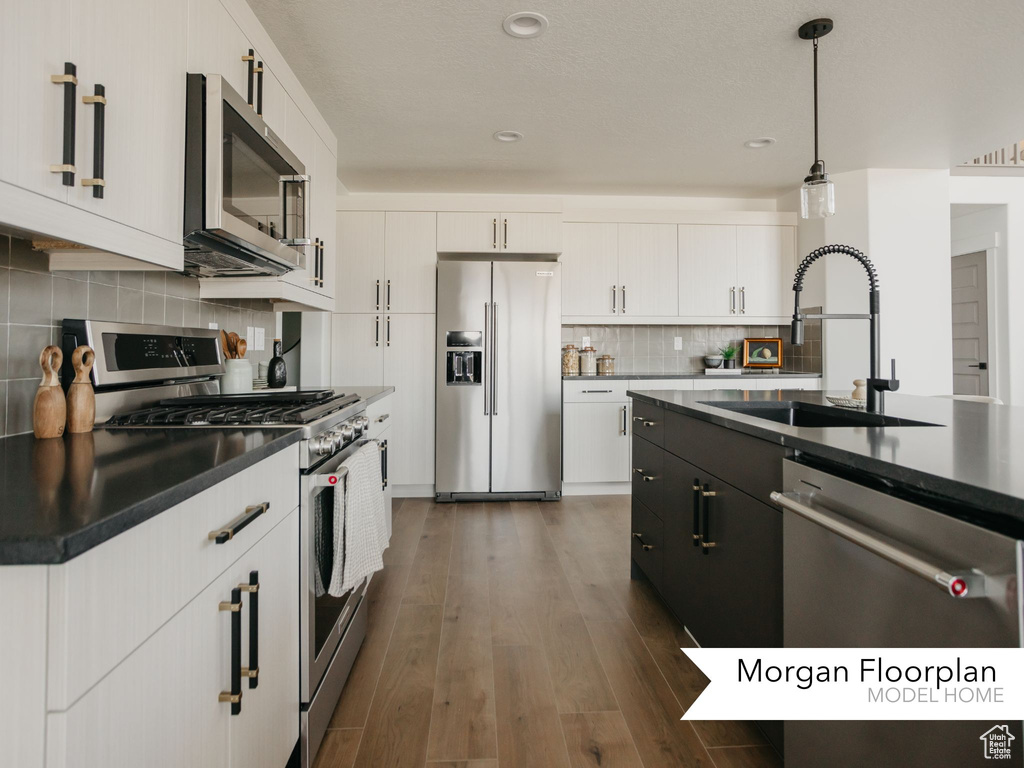 Kitchen with appliances with stainless steel finishes, a sink, dark countertops, decorative backsplash, and white cabinetry