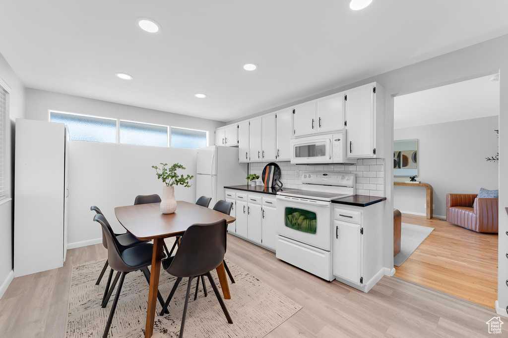 Kitchen with white appliances, dark countertops, tasteful backsplash, white cabinets, and light wood-type flooring