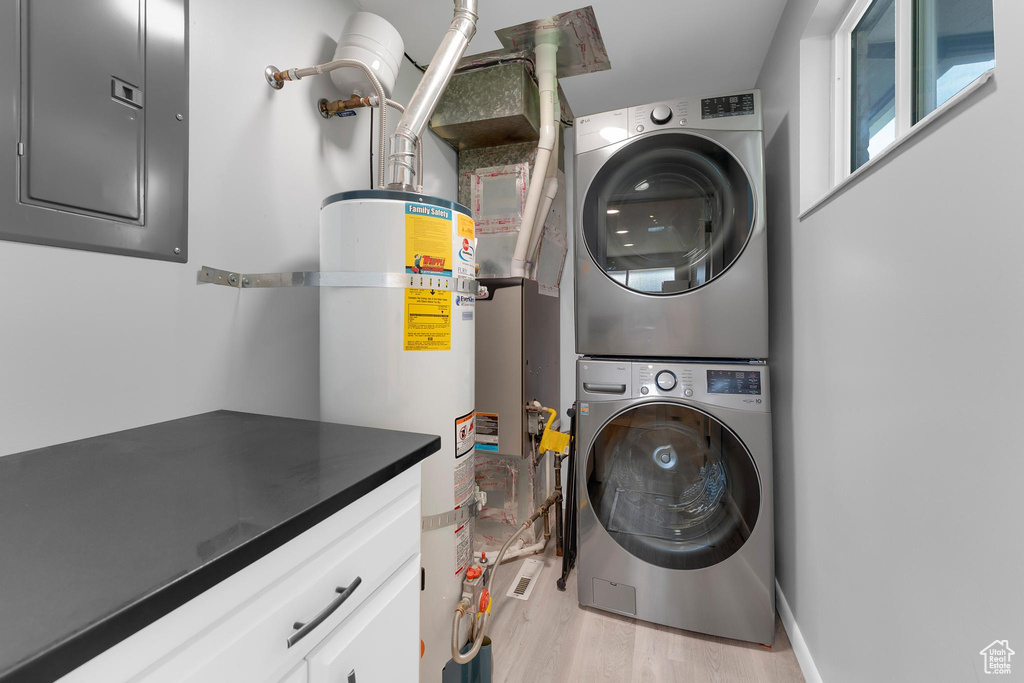 Laundry area with estacked washer and dryer, electric panel, strapped water heater, cabinet space, and light wood-style floors