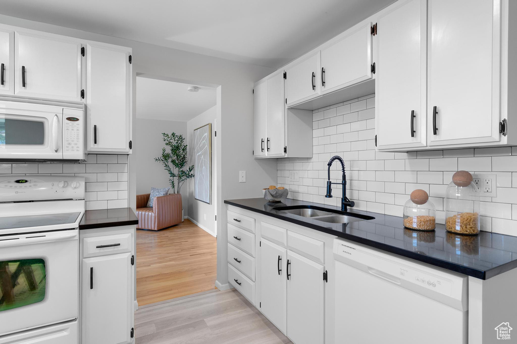 Kitchen featuring white appliances, a sink, dark countertops, light wood-style floors, and white cabinetry