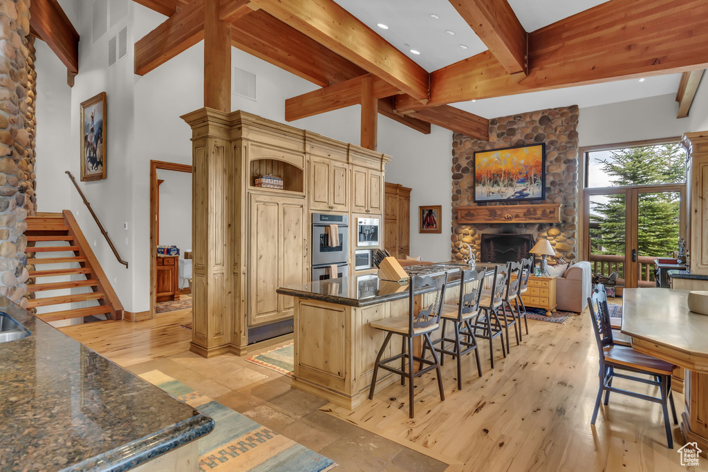 Kitchen featuring beamed ceiling, a stone fireplace, a kitchen bar, a towering ceiling, and a kitchen island