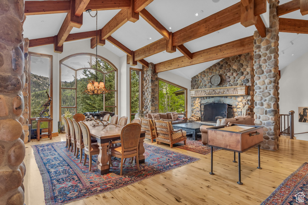 Dining area with beam ceiling, wood-type flooring, a chandelier, a stone fireplace, and high vaulted ceiling