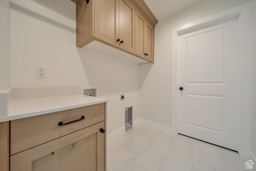 Laundry room featuring light marble finish flooring, hookup for an electric dryer, cabinet space, washer hookup, and baseboards